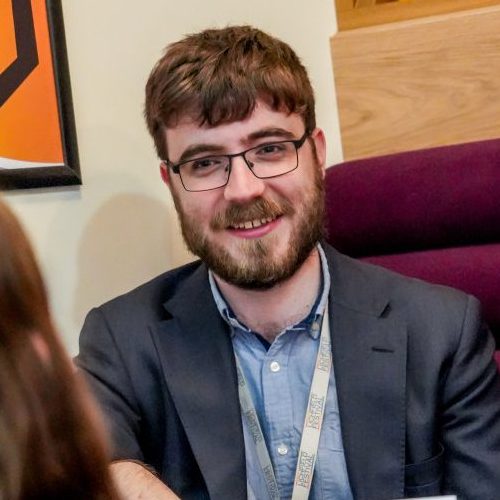 A man with brown hair and a beard in a suit jacket