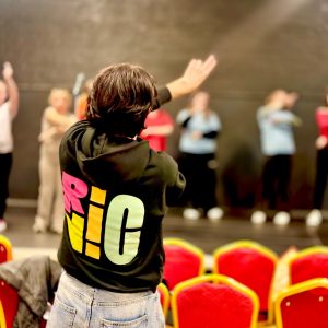 A staff member wearing a RicNic Hoodie directs a group of people on stage