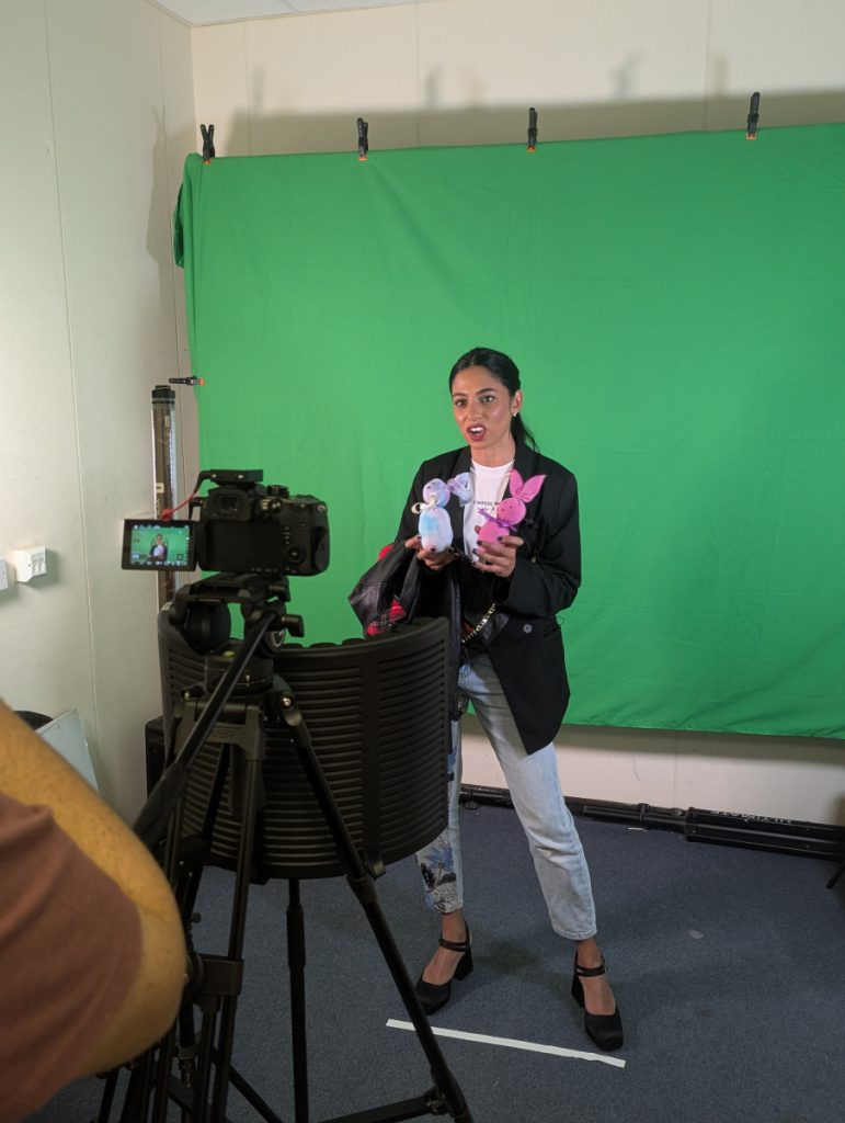 A designer holds some sock dolls in front of a green screen