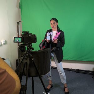 A designer holds some sock dolls in front of a green screen